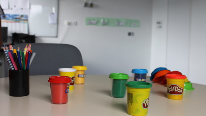 Photographie d'un pot de crayons de couleurs et de pots de pate à modeler posés sur une table.